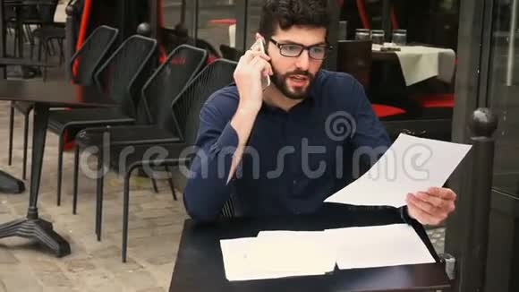商人用智能手机争吵在咖啡馆的桌子上看报纸视频的预览图