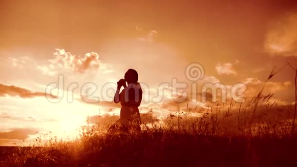 女孩在日落时双手交叉祈祷剪影生活方式女人跪着祈祷慢动作视频女孩视频的预览图