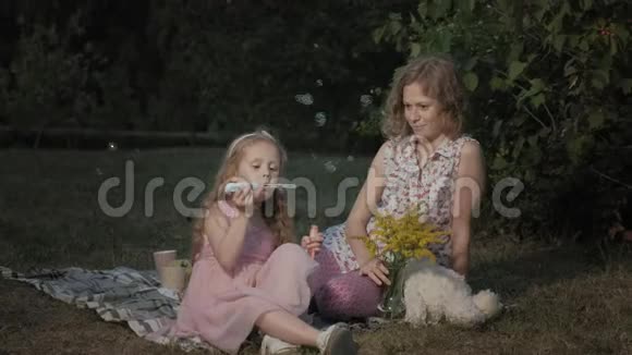一对幸福的母女给肥皂泡充气一家人在城市公园里在日落的温暖的晚上野餐视频的预览图