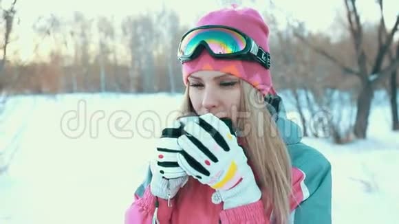 女人手里拿着热水瓶里的杯子在雪白的树枝上喝茶视频的预览图