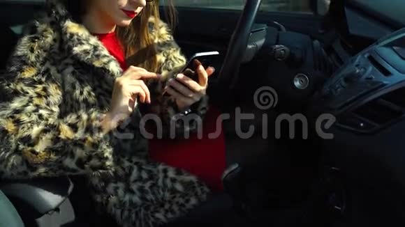 漂亮的女人穿着毛皮外套用智能手机在车里喝咖啡视频的预览图