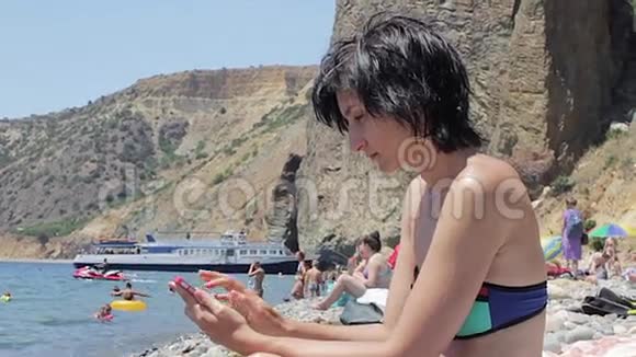 有魅力的女人在海滩上使用智能手机视频的预览图