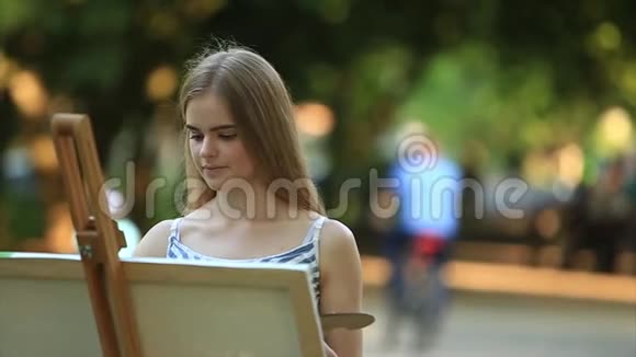 美丽的女孩站在公园里用颜料和铲子画一幅画视频的预览图