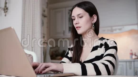 一位美丽的年轻黑发女人的肖像在明亮的餐厅里使用笔记本电脑视频的预览图