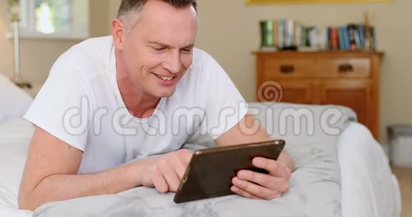 男子在床上放松时使用数码平板电脑视频的预览图