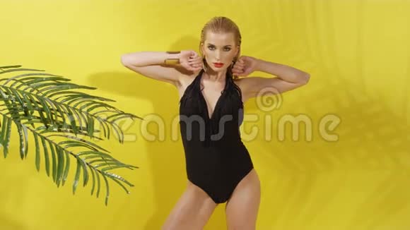 美丽的年轻女子在黄色背景下穿着黑色泳衣视频的预览图