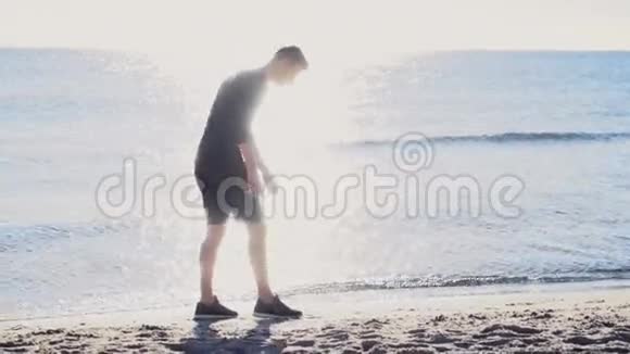 男跑运动员在阳光下缓慢地在海滩上系鞋带视频的预览图