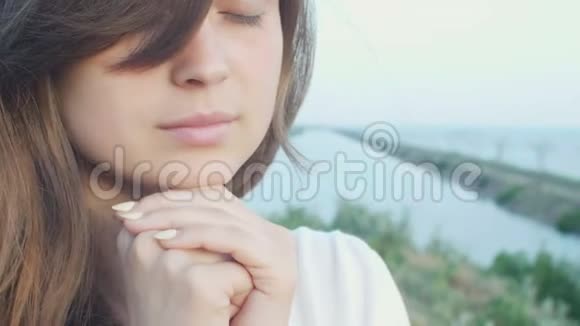 年轻美丽的女人在大自然中转向上帝女孩祈祷时双手交叉在下巴宗教观念视频的预览图