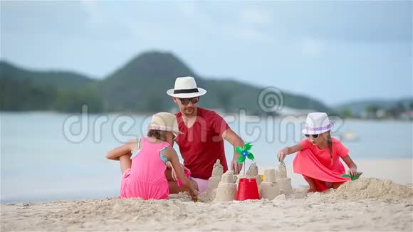 父亲和两个女孩在热带海滩玩沙子做沙堡视频的预览图