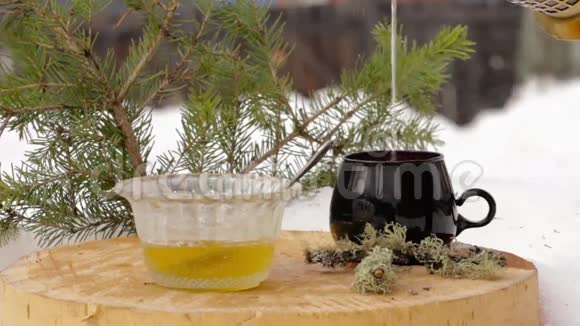 带蜂蜜的茶具把热茶从透明的茶壶倒到雪中的黑杯子视频的预览图