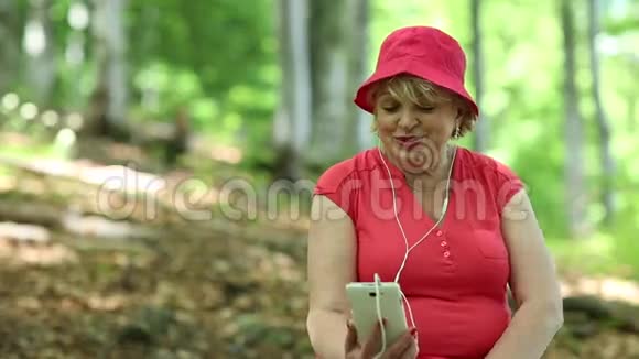 女人坐在森林中一棵倒下的树上通过智能手机进行交流视频的预览图
