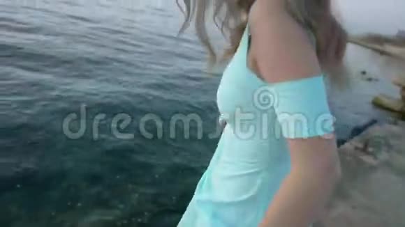穿着蓝色裙子的漂亮女孩站在海边摆姿势视频的预览图