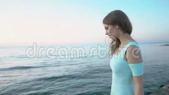穿着蓝色裙子的漂亮女孩站在海边摆姿势视频的预览图