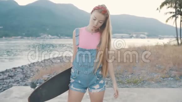 美丽而时尚的年轻女性在海边摆着一个长板视频的预览图