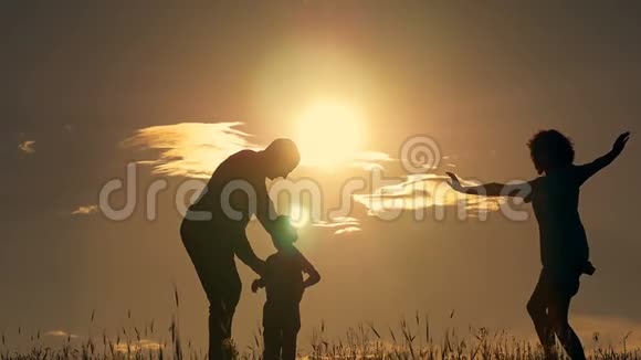 幸福的年轻家庭孩子们在田野里奔跑夕阳下的剪影视频的预览图