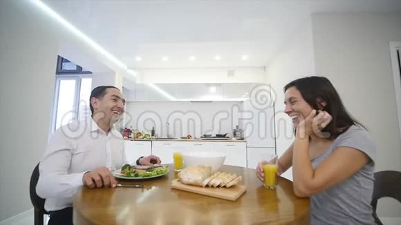 快乐的一对夫妻在厨房里一起聊天和吃早餐视频的预览图