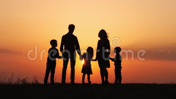 日落时幸福家庭的剪影在草地上牵手视频的预览图