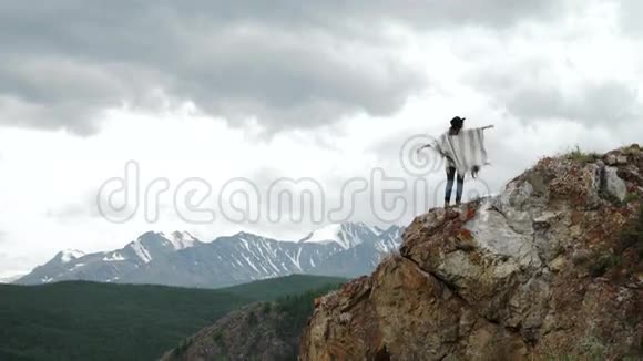 年轻漂亮的女旅行者戴着帽子和斗篷在山顶上放松群山环绕视频的预览图