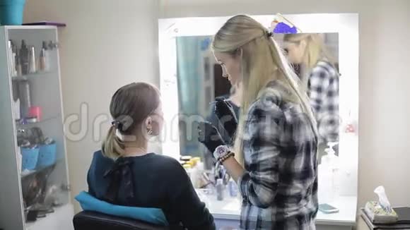化妆师和模特年轻的金发女郎化妆师用专业的刷子给一个漂亮的女孩画眉毛视频的预览图