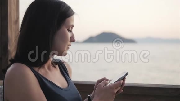 年轻的布鲁内特在日落时分坐在海边的咖啡馆里使用她的智能手机视频的预览图