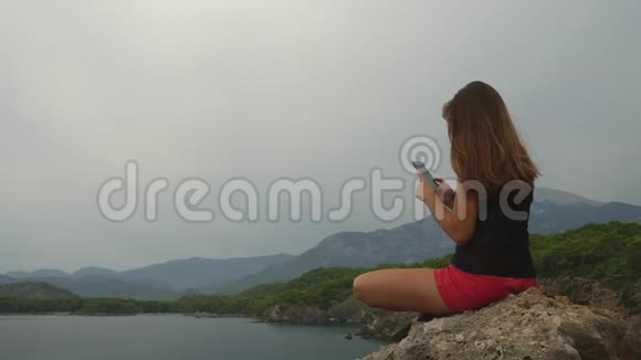 女游客坐在晴朗的天空和平静的海洋背景上的岩石上视频的预览图
