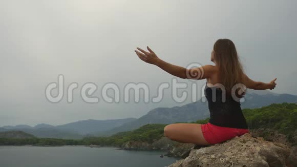 女游客坐在晴朗的天空和平静的海洋背景上的岩石上视频的预览图