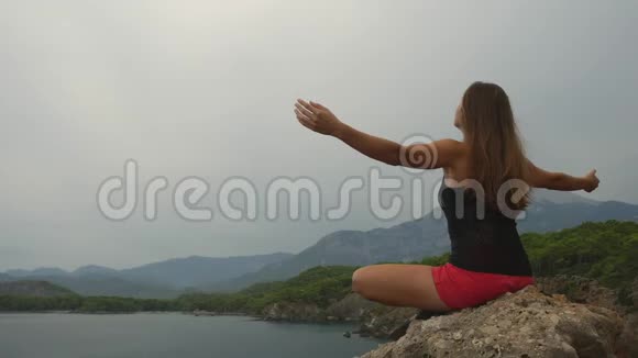 女游客坐在晴朗的天空和平静的海洋背景上的岩石上视频的预览图