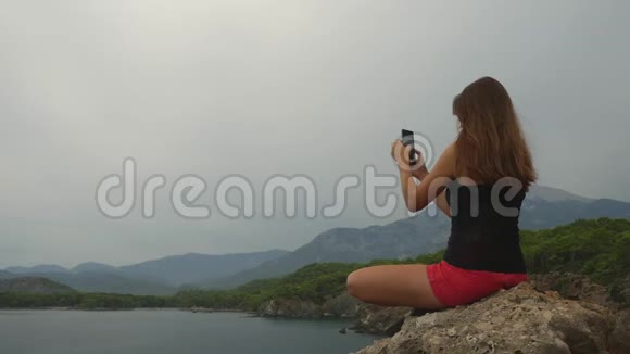 女游客坐在晴朗的天空和平静的海洋背景上的岩石上视频的预览图