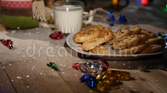 木制棕色桌子上面装饰着圣诞用品和花环圣诞节时一杯牛奶和一盘饼干视频的预览图