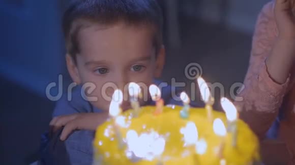 一个小男孩看着节日蛋糕上的蜡烛许愿视频的预览图