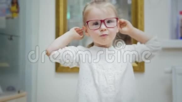 小女孩在眼科诊所镜子附近试戴眼镜视频的预览图