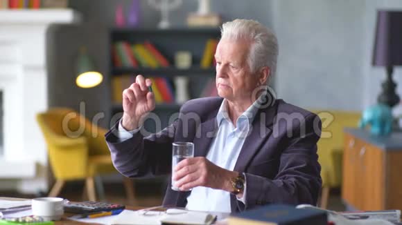 不高兴的悲伤和烦恼的老人看着一颗药丸吃了它视频的预览图