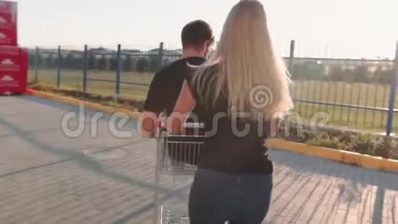 日落时分年轻的女人在超市停车场的手推车里翻滚着迷人的家伙慢动作视频的预览图