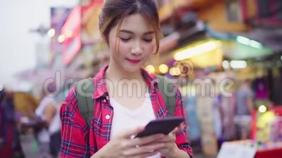 亚洲女性游客背包客微笑并使用智能手机独自旅行户外城市街道视频的预览图
