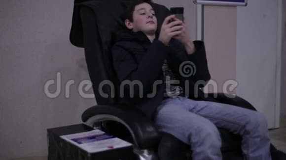 青少年坐在按摩椅上拿着智能手机视频的预览图