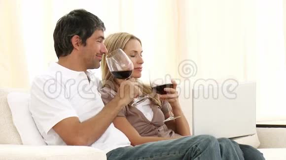 一对夫妇拿着笔记本在沙发上喝酒视频的预览图