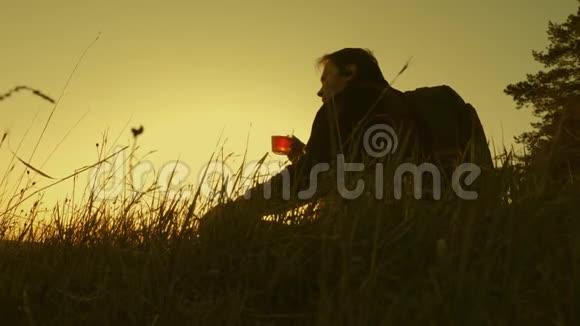 旅行者坐在山顶上用热水瓶喝咖啡游客喝热茶看日落概念视频的预览图