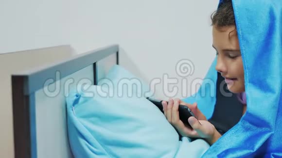 带智能手机的毯子下可爱女孩的肖像在社交媒体毯子下玩网络游戏的小女孩视频的预览图