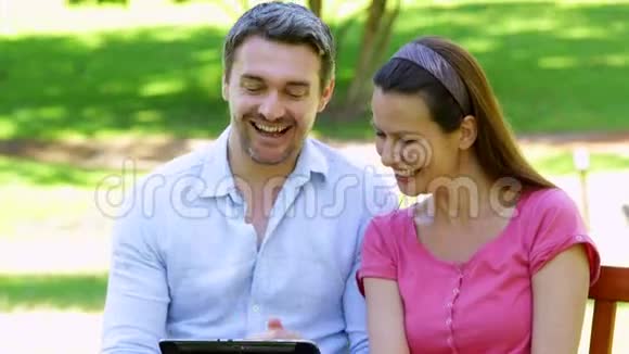 使用平板电脑坐在公园长椅上的幸福夫妇视频的预览图