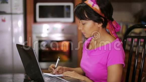 有笔记本电脑的女人从厨房的互联网上写食谱视频的预览图