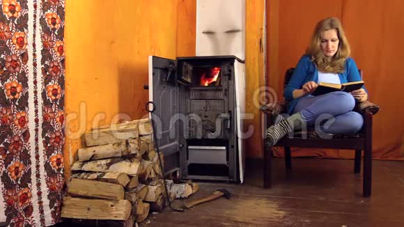 女人坐在家里的扶手椅上在火炉旁看书视频的预览图