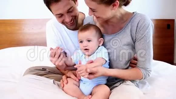 快乐的父母和他们的小儿子坐在床上视频的预览图