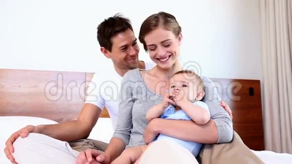 快乐的父母和他们的小儿子坐在床上视频的预览图