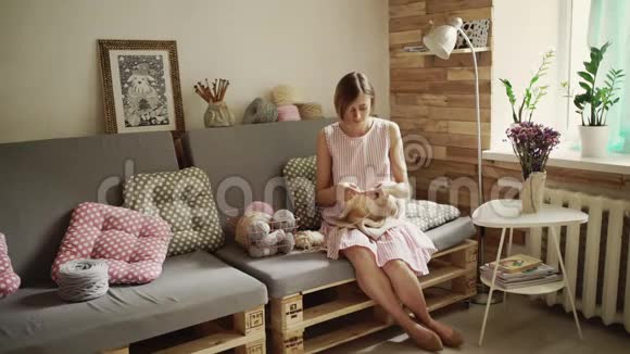 有创意的女人坐在沙发上编织羊毛衣服视频的预览图