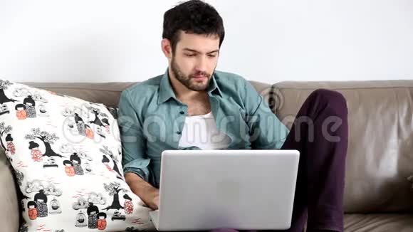 年轻的帅哥坐在沙发上膝上有笔记本电脑视频的预览图