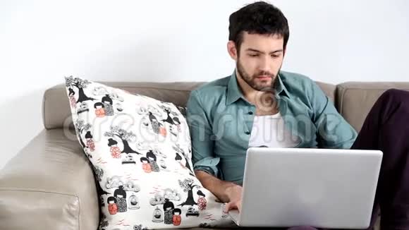 年轻的帅哥坐在沙发上膝上有笔记本电脑视频的预览图