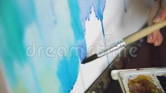 年轻的女画家用水彩画和画笔在画架画布上画特写视频的预览图
