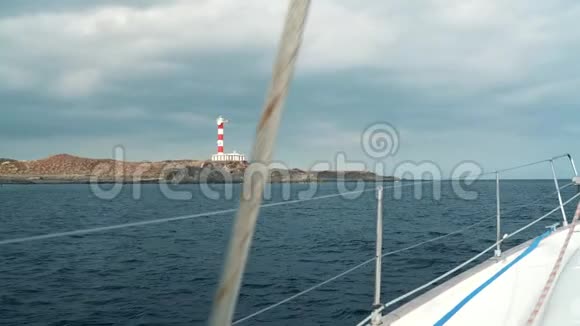 一位戴着黄色帽子穿着蓝色裙子的女士在海洋的夏季靠近灯塔的游艇上休息视频的预览图