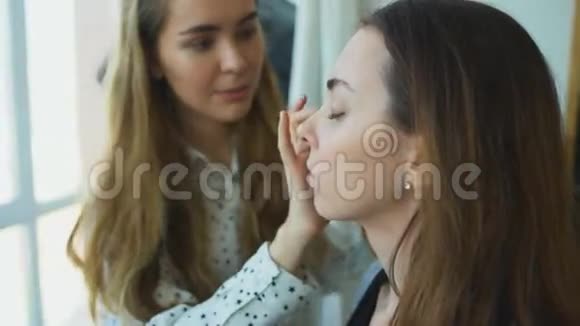 年轻的化妆师在一个重要的活动前为一个女孩做漂亮的化妆面部特写视频的预览图