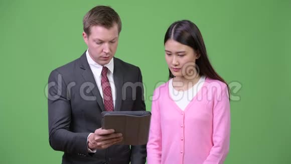 年轻的亚洲妇女和年轻的商人一起使用数字平板电脑视频的预览图